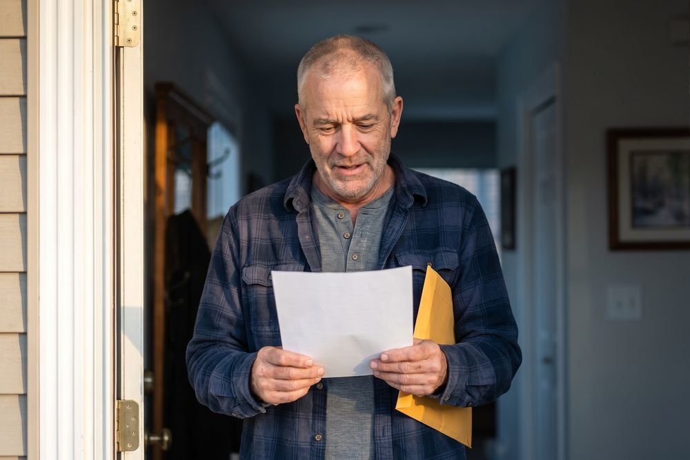 A man in his sixties standing in his doorway reading a letter about his disability claim